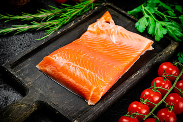 Salted salmon with greens and tomatoes on a cutting board.