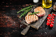 Grilled tuna steak on a cutting board with spices, tomatoes and rosemary. 