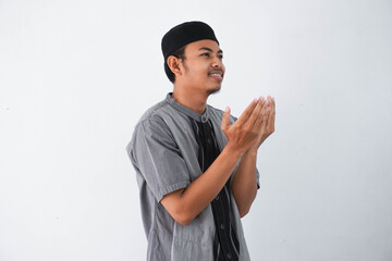 Religious young asian muslim man with open eyes praying, holding palms face up, whispering pray, isolated on white background. Religion islam, believing concept