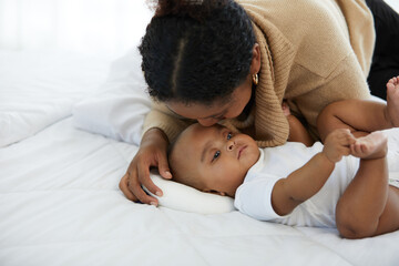 Wall Mural - African young mother kissing her infant baby lying on the bed