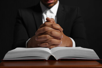Wall Mural - African American man with Bible praying to God at table on black background, closeup