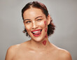 © K. A./peopleimages.com - Beauty, face and woman lipstick and wink with kiss print on skin, flirt and sexy, tongue out isolated on studio background. Red, lips and smile with skincare, makeup mockup, fun and cosmetic care