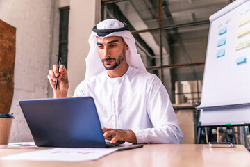 Wall Mural - Handsome arab businessman wearing emirates kandora working at computer latop at his desk in the office, Dubai