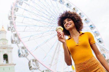 Beautiful young black woman eating ice cream at amusement park - Cheerful african-american female portrait during summertime vacation- Leisure, people and lifestyle concepts