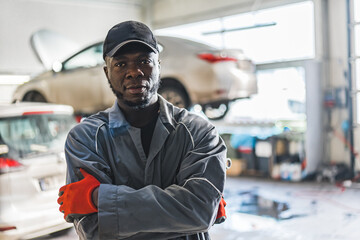 An auto mechanic wearing uniform gloves and a hat stands in a busy auto repair shop. High-quality photo