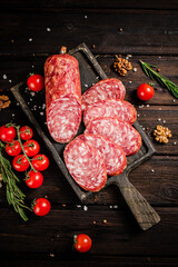 Wall Mural - Pieces of salami sausage on a cutting board with cherry tomatoes and rosemary.