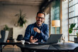 © bnenin - Portrait of a smiling male boss, holding a mobile phone, sitting at the office.