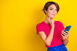 © deagreez - Photo of minded pretty lady wear pink stylish clothes hold device look empty space think buy novelty isolated on yellow color background