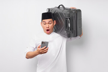 Surprised young Asian Muslim man carrying a suitcase and using mobile phone while reacting to bad news isolated on white background. Ramadan and eid Mubarak concept