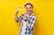 © Bangun Stock Photo - Excited Asian ethnicity young man 20s wearing casual clothes hat holding credit bank card, raising fist, celebrating success isolated on yellow background studio portrait. People lifestyle concept