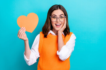 Sticker - Photo of lovely adorable impressed woman straight hairdo wear orange waistcoat hold heart hand on cheek isolated on teal color background