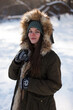 © Plutmaverick - A young girl, brunette, in sweater, a hat and an green jacket, against the backdrop of the winter landscape. Snow and frost, the concept of Christmas.