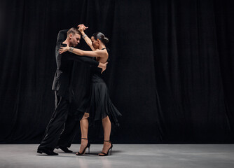 Passionate connection. Man and woman, professional tango dancers performing in black stage costumes over black background. Concept of hobby, lifestyle, action, motion, art, dance aesthetics