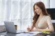 © ArLawKa - Asian businesswoman working with financial documents and laptop Inside office worker calculating financial indicators smiling and happy with success and results of business success