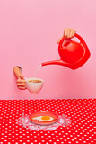 Fototapeta Kawa jest smaczna - Food pop art photography. Female hand sticking out pink paper, pouring milk into coffee cup over plate with fried egg. Concept of taste, creativity, art. Complementary colors. Copy space for ad, text