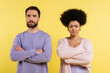 © LIGHTFIELD STUDIOS - displeased interracial couple standing with crossed arms while looking at camera isolated on yellow.