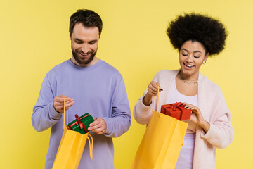 Wall Mural - happy interracial couple in stylish clothes holding shopping bags and presents isolated on yellow.
