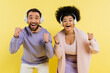 © LIGHTFIELD STUDIOS - excited interracial couple in wireless headphones showing yeah gesture isolated on yellow.