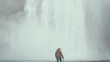Back view of young stylish man standing near the powerful waterfall in Iceland and looking at the falling water.