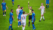 © Gorodenkoff - Soccer Football Championship Match: Referee Sees Foul, Gives Signal and Yellow Card, Players Circle him Upset. International Tournament. Sports Broadcast Channel Television Concept.