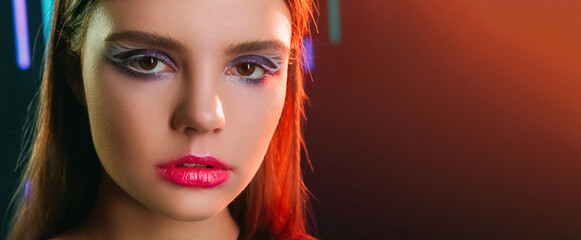 90s face. Retro makeup. 2000s fashion. Red color neon light closeup portrait of teen girl model with purple eyeshadow pink lips artistic look on dark copy space background.