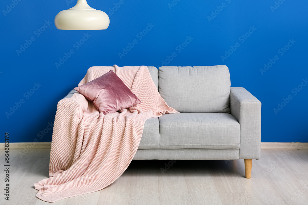 Grey sofa with cushion, plaid and hanging lamp near blue wall
