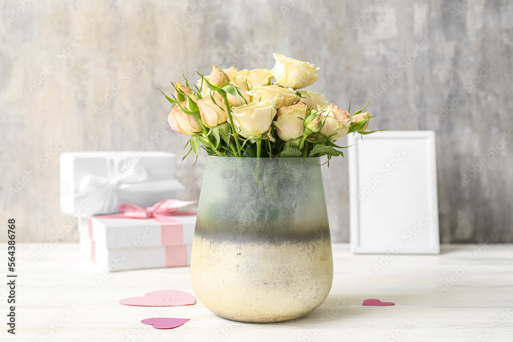 Vase with beautiful rose flowers on light wooden table near grunge wall