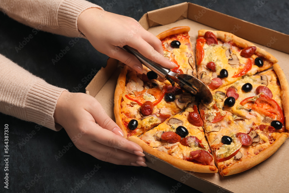 Woman cutting tasty pizza on dark background, closeup