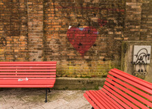 Old Brick Wall With Red Heart Graffiti And Red Benches In Italy