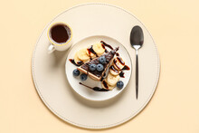 Table Setting With Piece Of Birds Milk Cake, Blueberries, Chocolate Topping, Banana Slices, Cup Of Coffee And Spoon On Beige Background