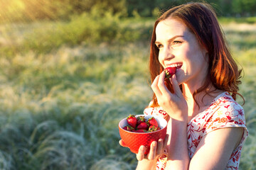 Cheerful girl enjoying strawberry on nature background. Slim woman eats berries. Healthy lifestyle wellness