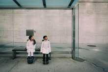 Two Asian Girls Dressed In Winter Clothe Sitting At A Bus Stop In The City