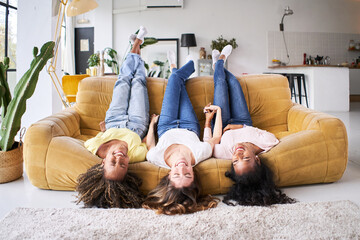 Wall Mural - Three mixed race multi ethnic female best friends laugh good happy at sofa home. Cheerful women having fun in amazing loft enjoying life style in living room. Girlfriends affectionate. High quality