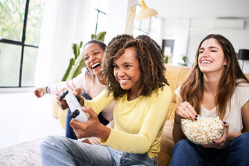 Wall Mural - Group of young female multiracial young friends play video games together at home. Only women gaming and eating popcorns. . High quality photo