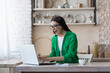 © Liubomir - A young woman is sitting at home in the kitchen using a laptop. Plays online games, lottery, raffle. Celebrates victory, rejoices in winning