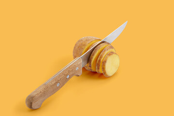 Wall Mural - Knife slicing potato on yellow pastel background