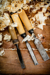 Chisels with wooden shavings. On a wooden background.