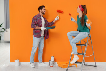 Wall Mural - Man painting orange wall and happy woman holding can of dye with brush indoors. Interior design