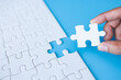 © Tinnakorn - Hand put last piece of jigsaw puzzle. White unfinished jigsaw puzzle on  blue background.The correct solution. Teamwork, Solving and completing the task. Assembling jigsaw puzzle pieces.