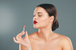 © Allistair F/peopleimages.com - Lipstick, woman and makeup in studio for skincare, cosmetics and aesthetics. Young model face, red colorful lips and beauty product for luxury fashion, salon and cruelty free facial balm application