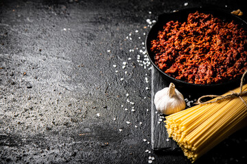 Wall Mural - Bolognese sauce on a stone board with a bunch of dry pasta and garlic. 