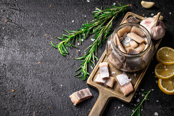 Canvas Print - Salted herring in a jar on a cutting board with rosemary and lemon. 