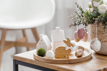 A beautiful postcard. The concept of the Bright Easter holiday. Flowers, rabbits, Easter eggs and Scandinavian white houses on a wooden table in a cozy living room.