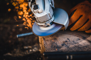 The hands of the master saw the metal with a grinder. Metal works in the workshop close up. Metal processing with angle grinder. Sparks in metalworking.