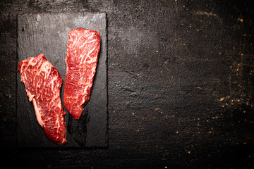 Poster - Raw steak on a stone board. On a black background.