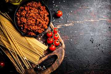 Poster - Bolognese sauce on a cutting board with cherry tomatoes and dry pasta. 