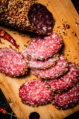 Poster - Pieces of salami sausage on a cutting board with pods of dried chili peppers. 