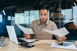 © Liubomir - Problem with documents at work. Upset young African-American businessman working in office, holding papers in hands, spreading hands, looking worriedly at camera.