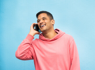 Poster - Casual man, phone call and laughing in communication standing isolated on a blue background. Happy male, person or guys with pink jacket in discussion, conversation or talking on mobile smartphone