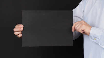 Wall Mural - Blank black board A4 paper in man hand covered face and wear blue shirt on black background..